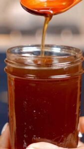 Overhead view of a glass jar filled with thinly sliced onions covered in golden honey, beginning to turn syrupy.